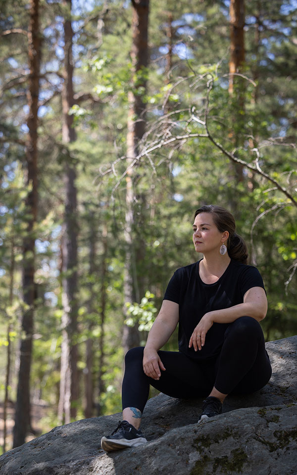 Emma William Olsson sitter på en stor sten i skogen.